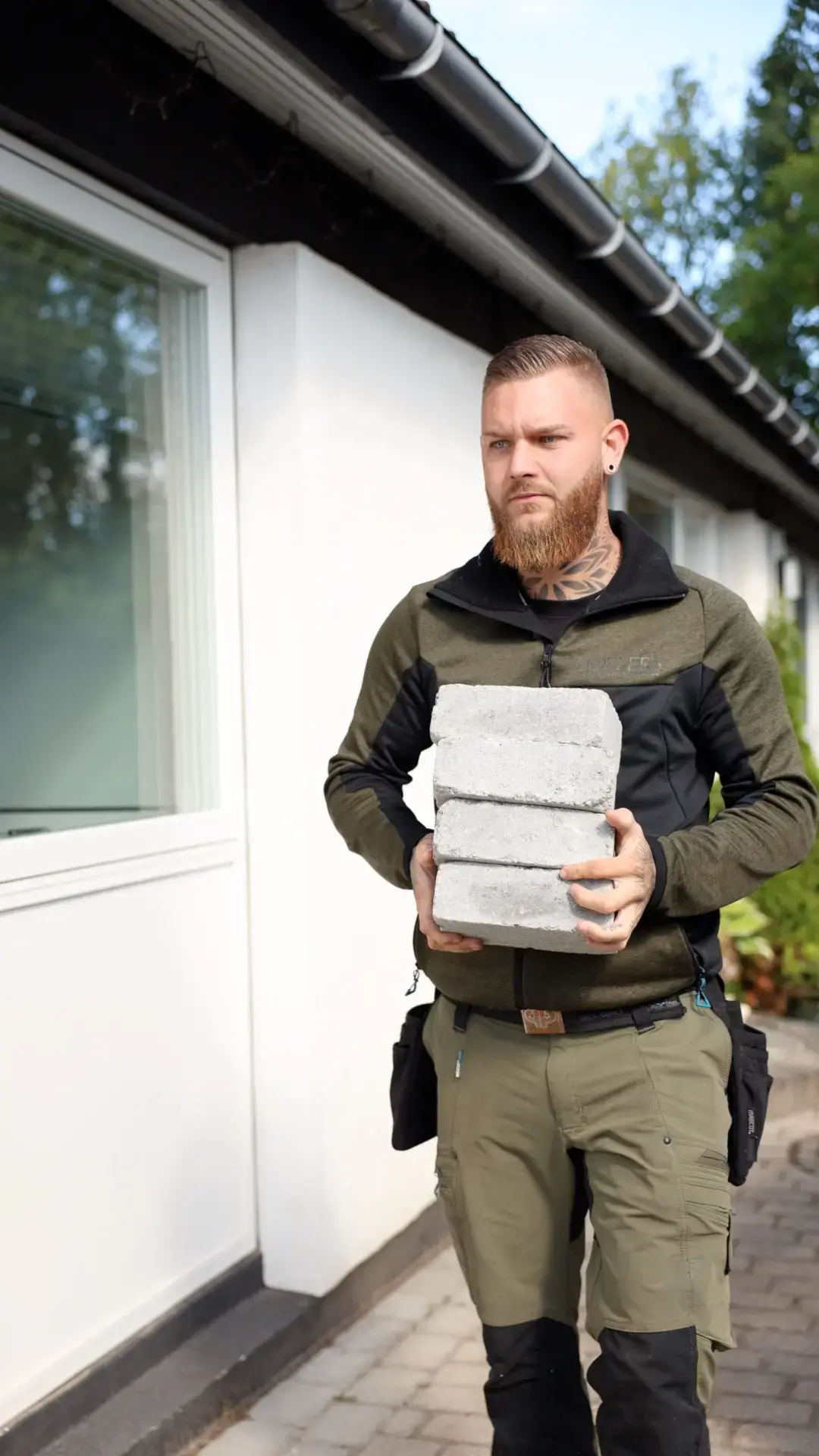 Mand med betonblokke udenfor ved hus, klar til opgaver.