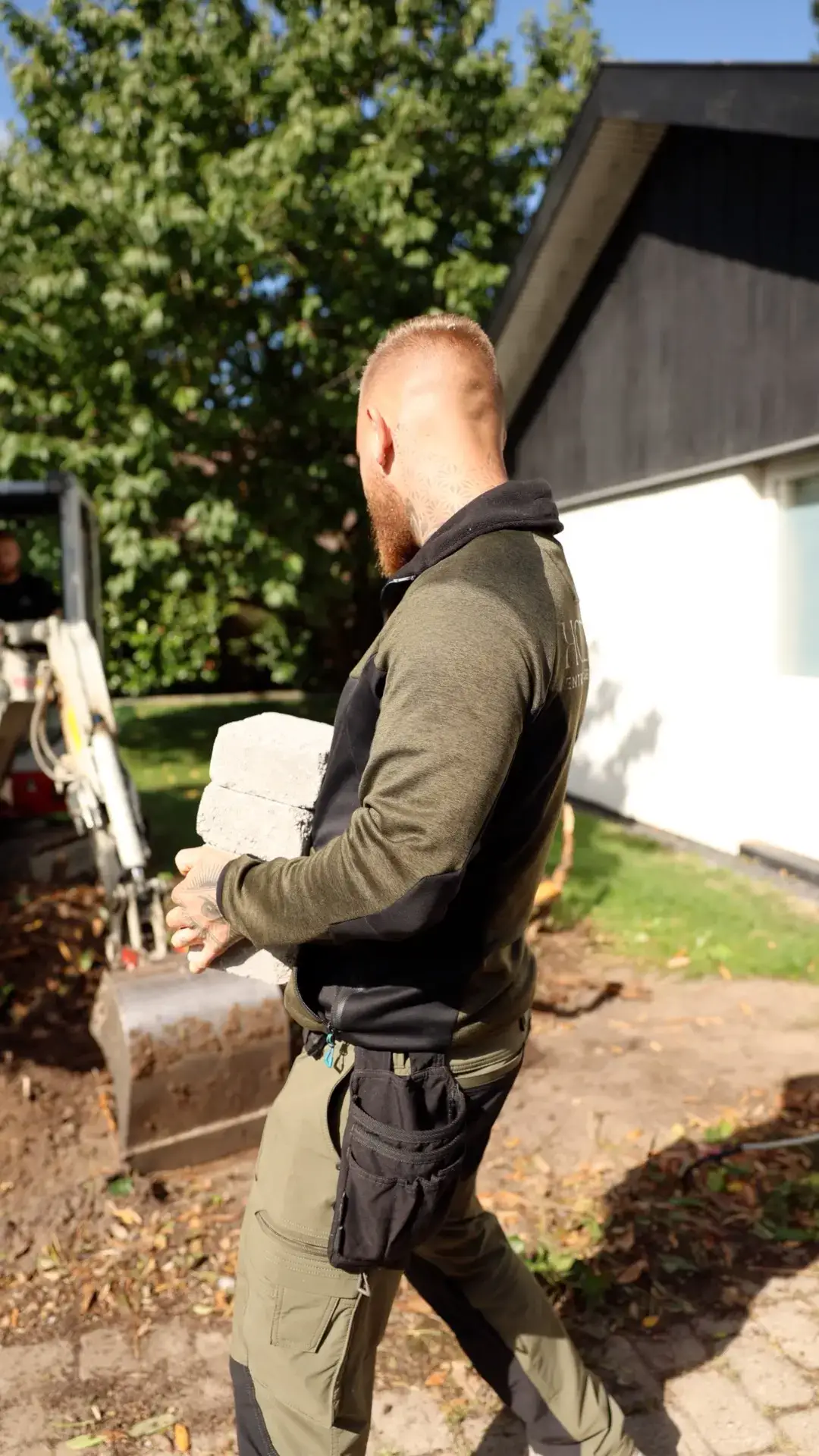 Mand med backpack, går i have med træer og hus i baggrunden.