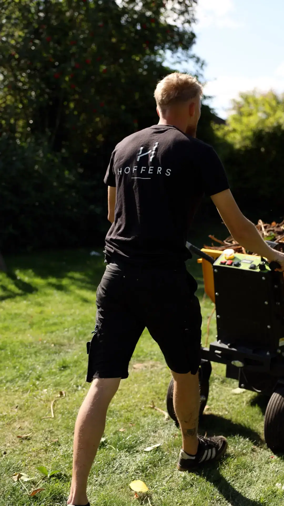 Hoffer medarbejder griller i haven med grilludstyr i solen.
